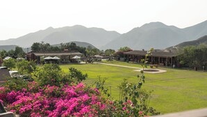 A hotel with a lawn, buildings, and mountains in the background. - Ranch Pachacamac (Pachacamac)