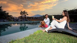 Two people sitting by a pool with a sunset view, lounge chairs, and a mountain in the background. - Ranch Pachacamac (Pachacamac)