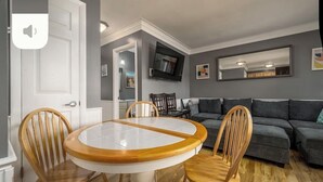 A dining area with a round table and four chairs, a gray sofa, and a flat-screen TV mounted on the wall. - 3 minutes to Beach, 2BD/2BA Near 28th St Boardwalk (Ocean City)