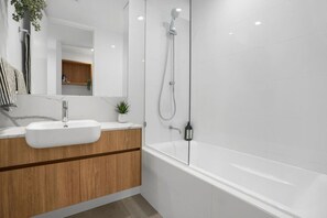 Une salle de bain moderne avec un lavabo blanc, un meuble-lavabo en bois, une cabine de douche en verre et une grande baignoire.