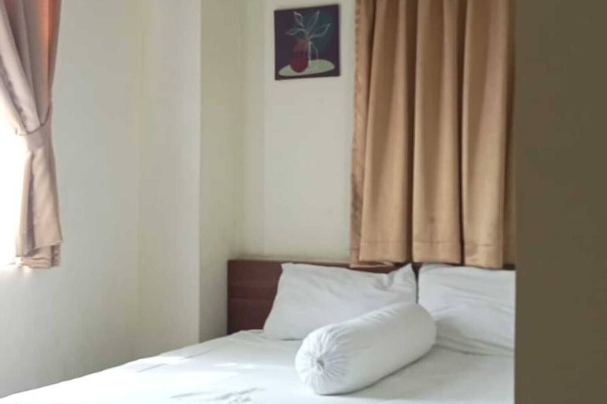 A hotel room with a bed, curtains, an air conditioning unit, and a wall-mounted picture.