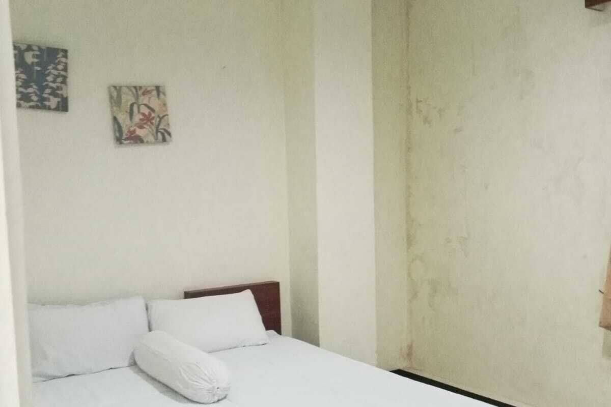 A single-bed room with a wooden headboard, white bedding, and two wall-mounted artworks.