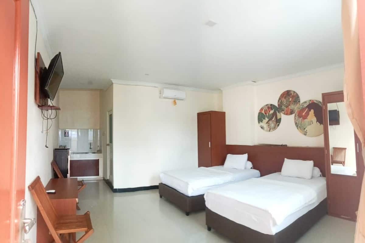 A hotel room with two beds, a dining table, a TV mounted on the wall, and a kitchen area in the background.