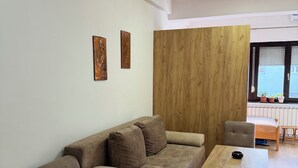 A modern living room with a brown sofa, a wooden coffee table, and a view of the outside through a window. - Sunny Cozy Studio • Wi-Fi • Elevator •Urban Studio (Skopje)
