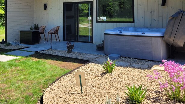 A modern house with a covered patio, a hot tub, and a garden with pebbles and plants.