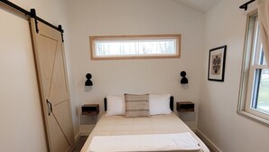 A bedroom with a bed, a window, a door, and a wall-mounted picture.