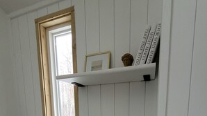 A room with a window, a shelf with books, a radio, and decorative items.