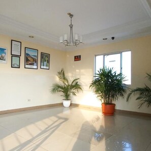 A spacious room with a high ceiling, a chandelier, framed pictures on the wall, and large windows allowing natural light. - Hotel Celebes (Manado)