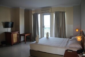 A hotel room with a bed, a desk, a television, and a balcony with curtains. - Hotel Celebes (Manado)