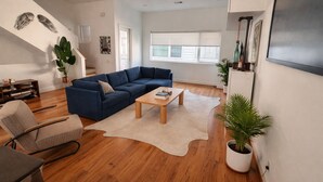 Un salon moderne avec un canapé d’angle bleu, une table basse en bois, un tapis blanc et une plante en pot.
