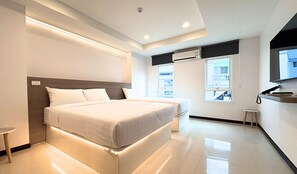 A modern hotel room with a large bed, a small bedside table, a built-in air conditioning unit, and a window with a view of a building. - Paul & Pam Hotel Bangkok (Bangkok)