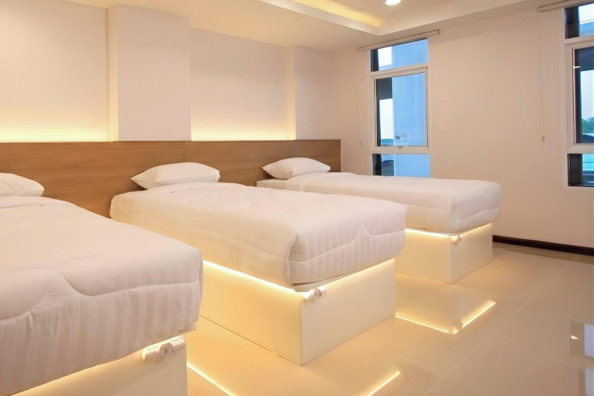 A hotel room with three beds, a wooden headboard, and a large window.
