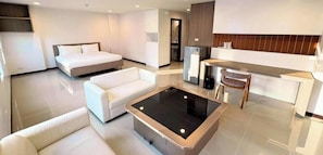 Una habitación de hotel moderna con cama, sofá, mesita de café, kitchenette y baño.