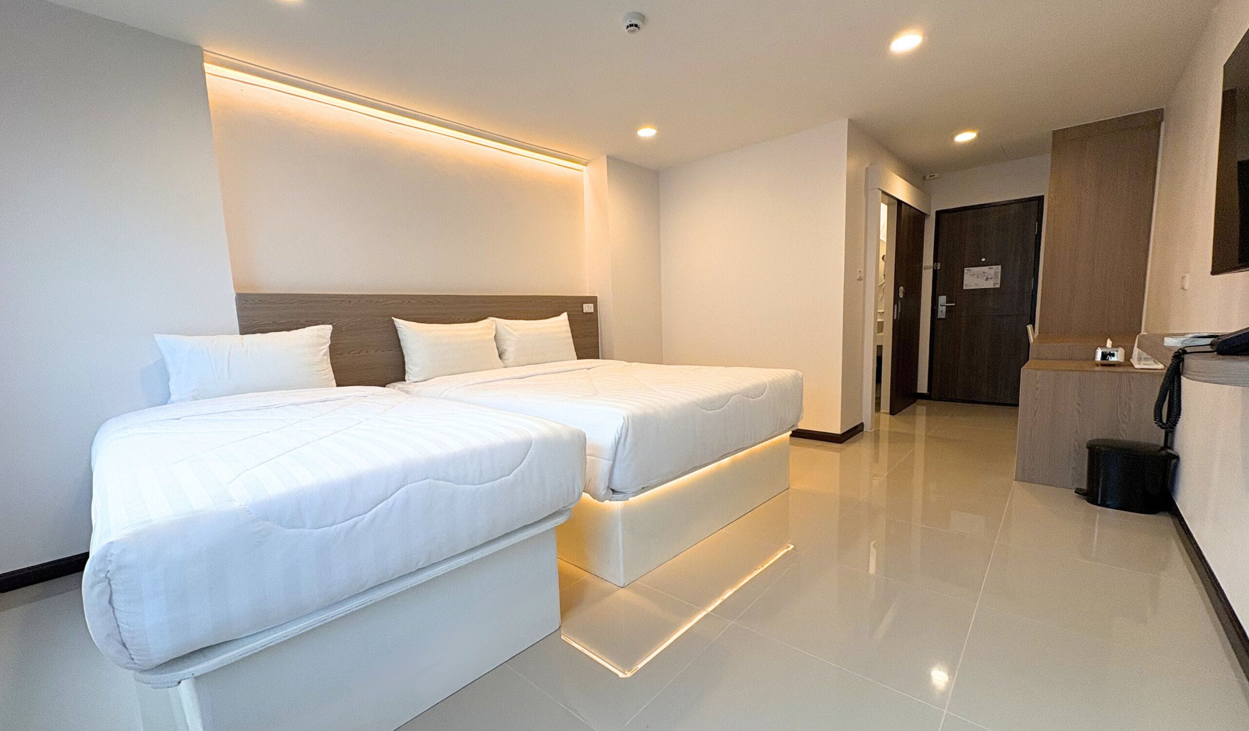 A hotel room with two beds, a wooden headboard, a small desk with a telephone, and a door leading to a bathroom.