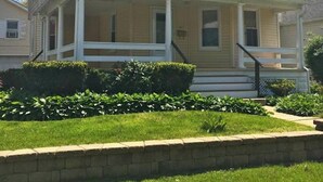 Una casa a due piani con un portico e un piccolo giardino antistante.