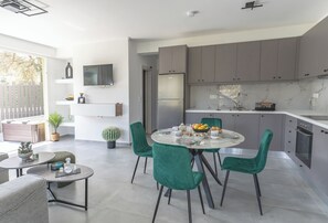 A modern kitchen with grey cabinets, a built-in fridge, and a dining area with a round table and green chairs. - Thyme Aroma - Quiet Nature Patio (Gonia, Rethymno Crete)