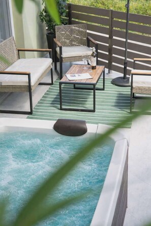Un bain à remous avec une table et des chaises en bois, un tapis à rayures vertes et une clôture en bois en arrière-plan.