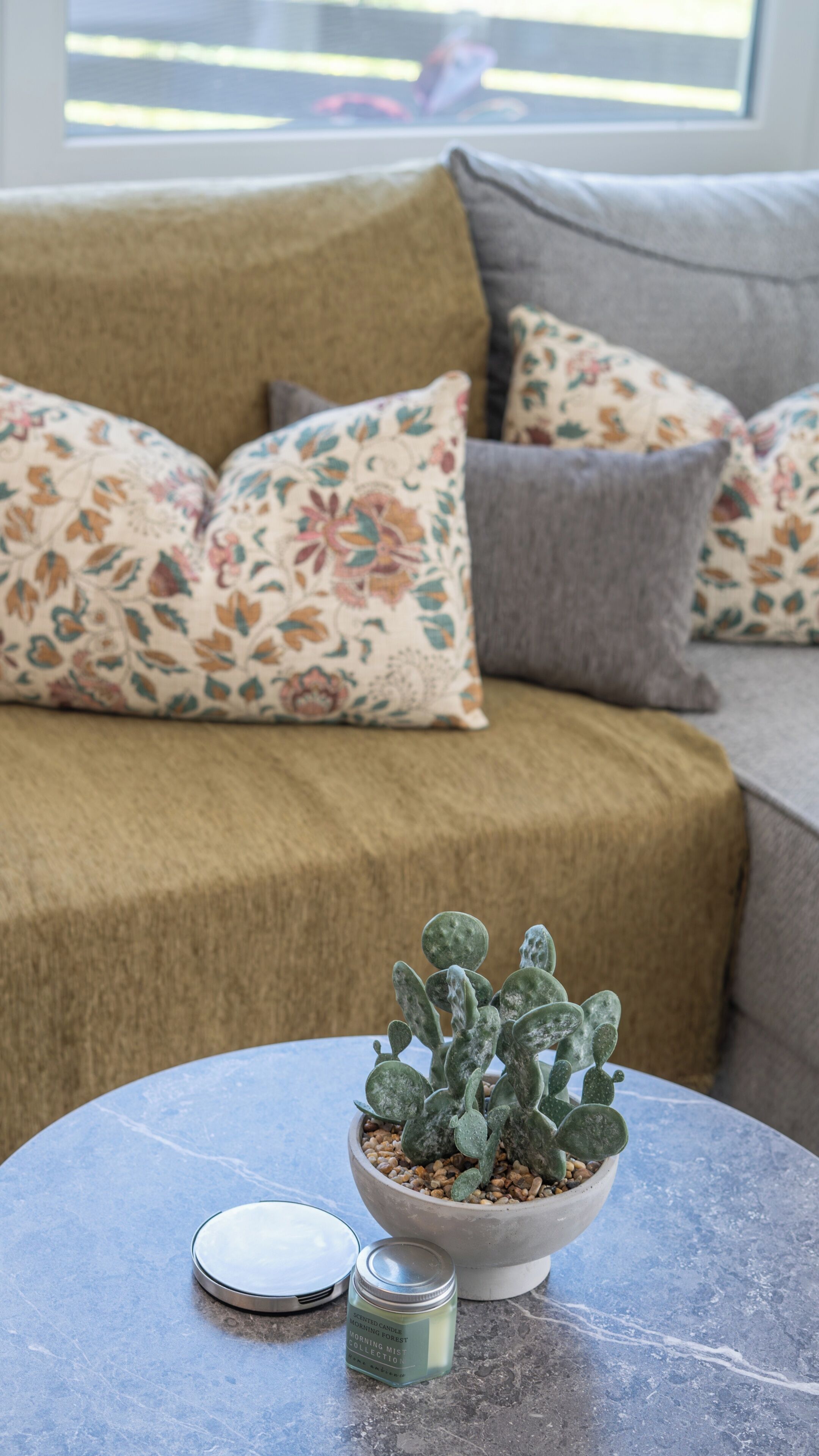 A room with a sofa, a table with a potted plant, and a candle.