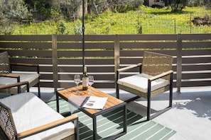 Un espace extérieur aménagé avec des meubles en osier, une table sur laquelle se trouvent une bouteille et des verres, et une vue sur un jardin.