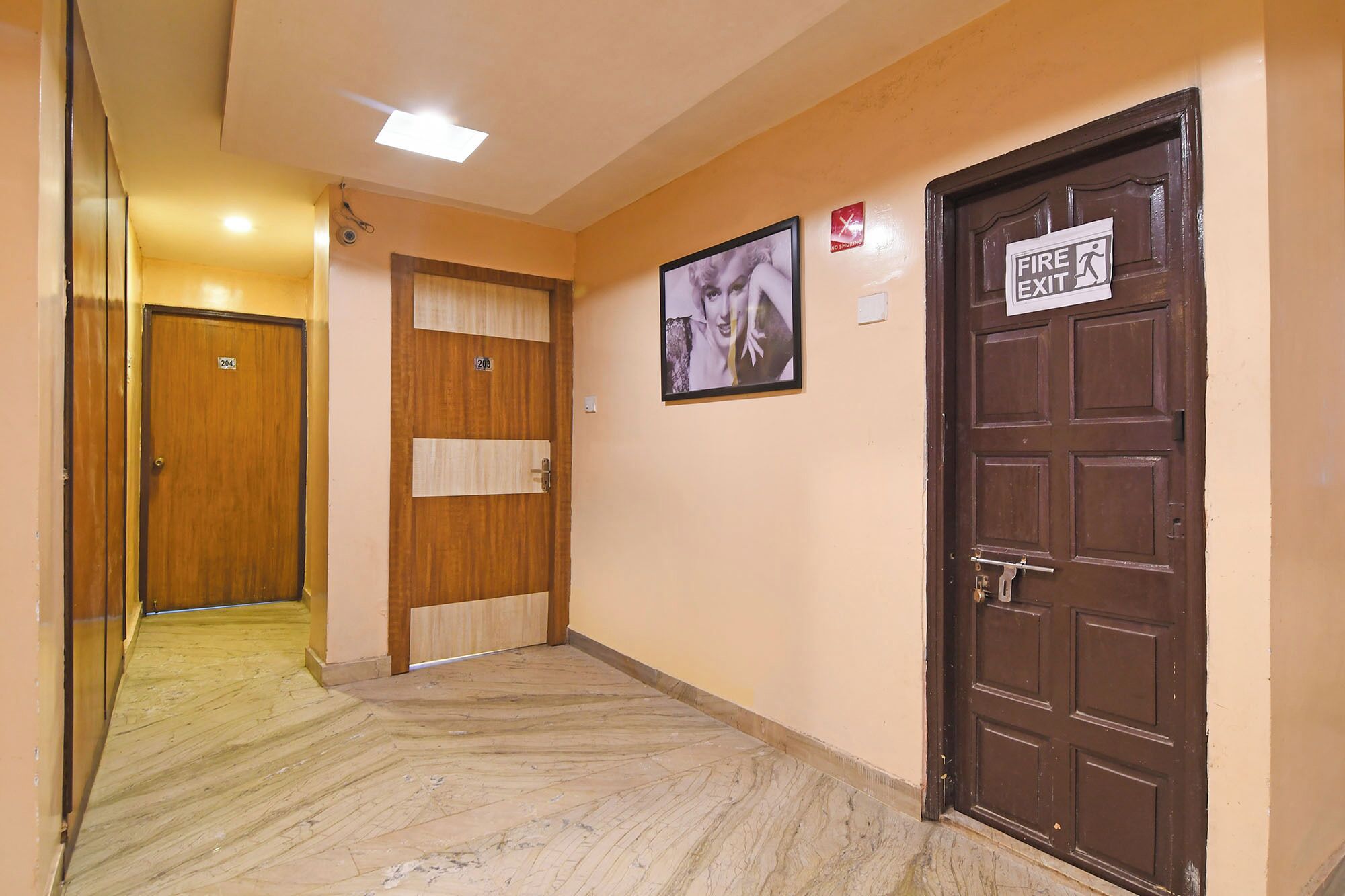 A hotel hallway with wooden doors, a fire exit sign, and a no smoking sign.