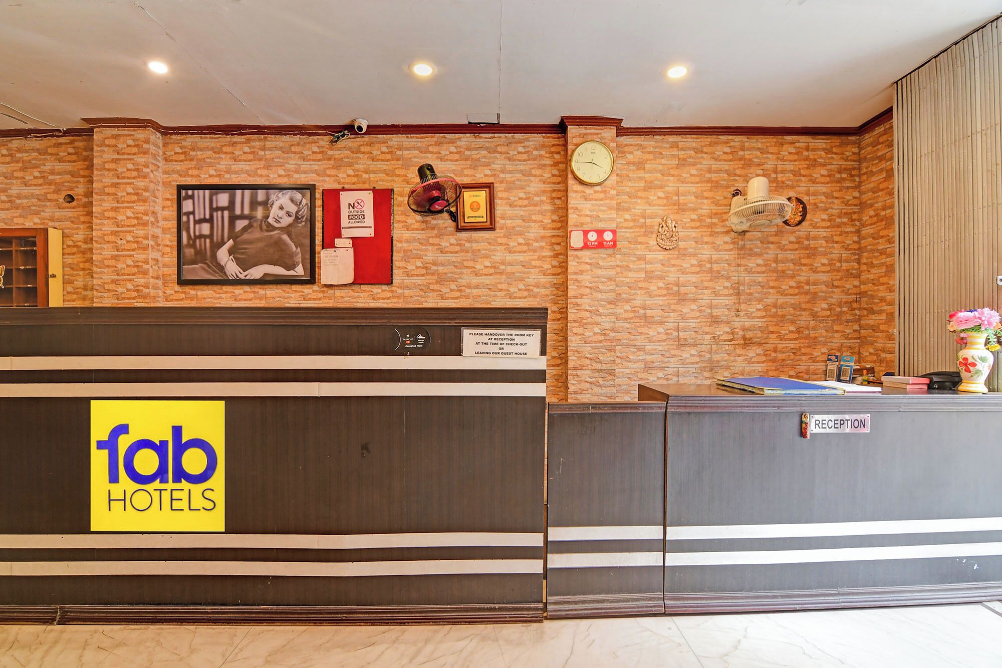 A hotel reception area with a reception desk, a clock, a 'No Outside Food' sign, and a 'Please Hand Over Room Key' sign.