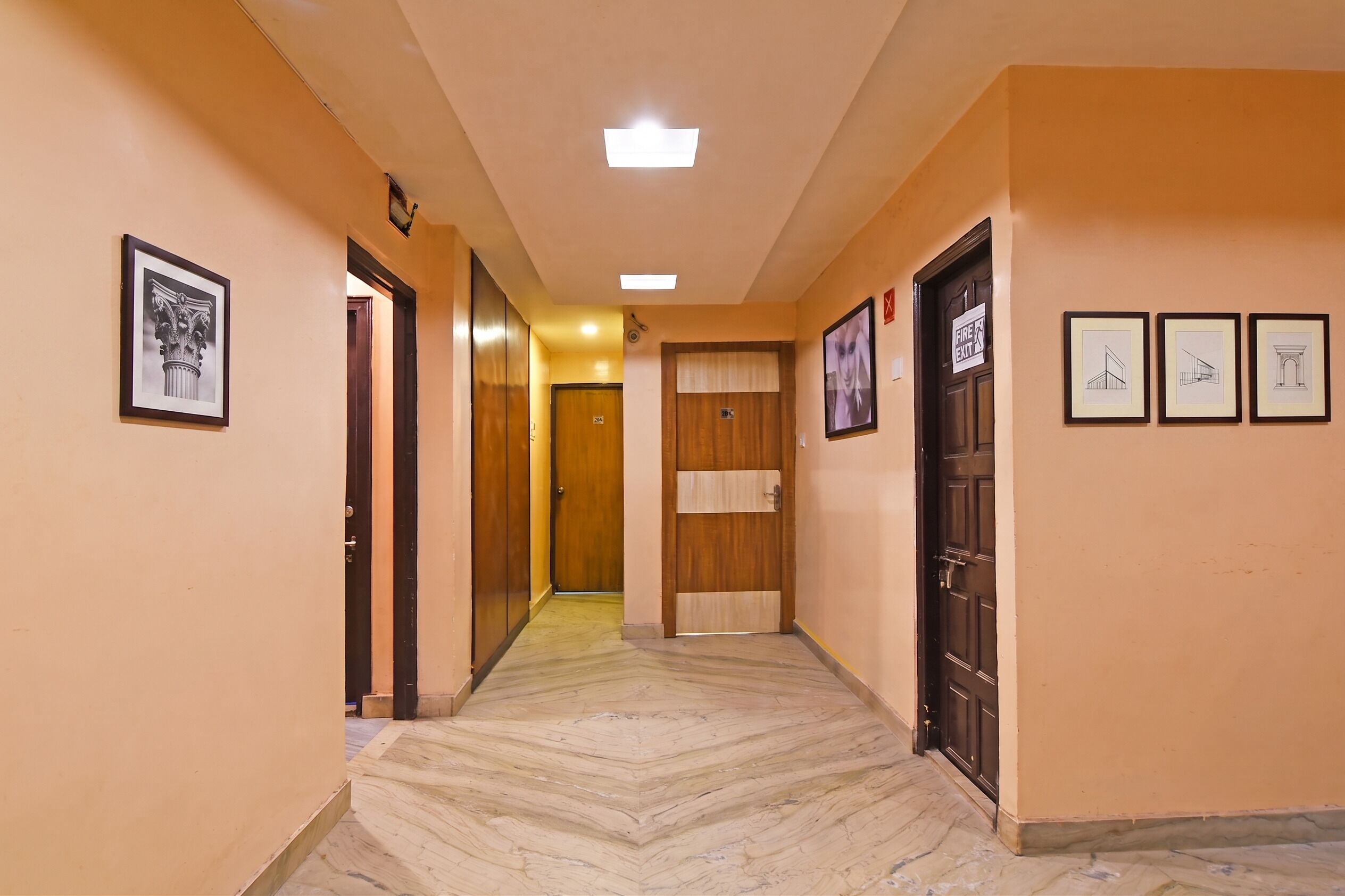 Un pasillo con puertas de madera, cuadros enmarcados y piso de mármol.