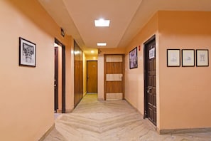 A hallway with wooden doors, framed artwork, and a marble floor. - Fabhotel Step Inn Stays (Kolkata)