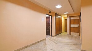 Un couloir doté d’un sol en marbre, de portes en bois et d’un luminaire au plafond.