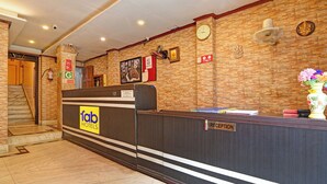 Un hall d’hôtel comprenant un comptoir d’accueil, une horloge, un ventilateur fixé au mur et un escalier menant à l’étage supérieur.