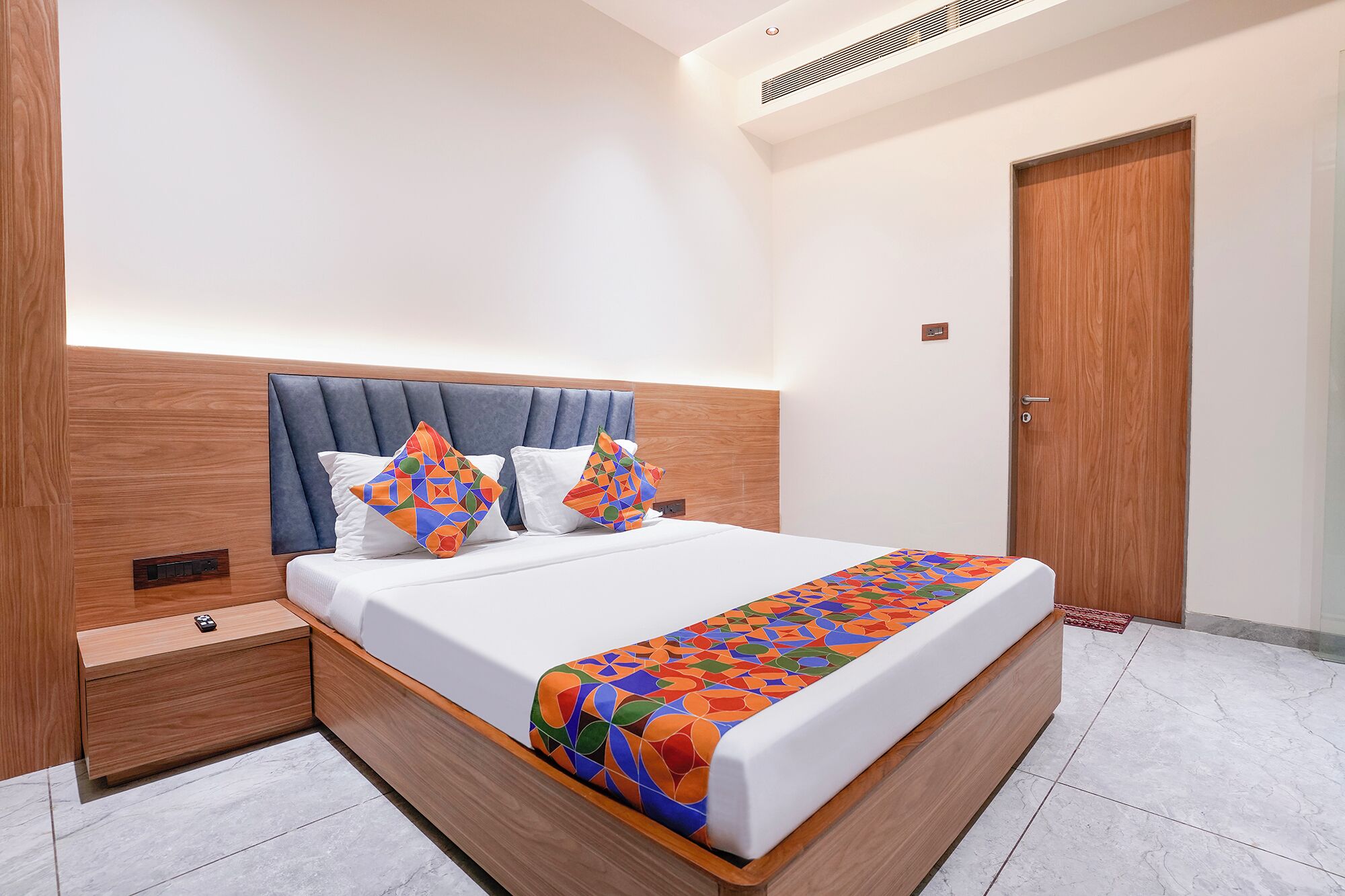 A modern hotel room with a large bed, wooden headboard, and a nightstand.