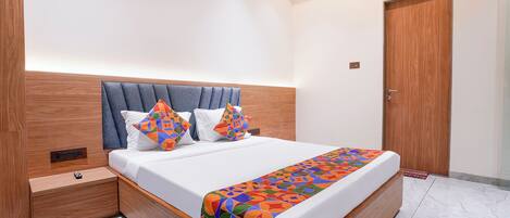 A modern hotel room with a large bed, wooden headboard, and a nightstand.