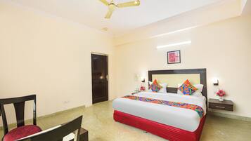 A hotel room with a bed, a chair, a ceiling fan, a door, and a nightstand with a lamp.