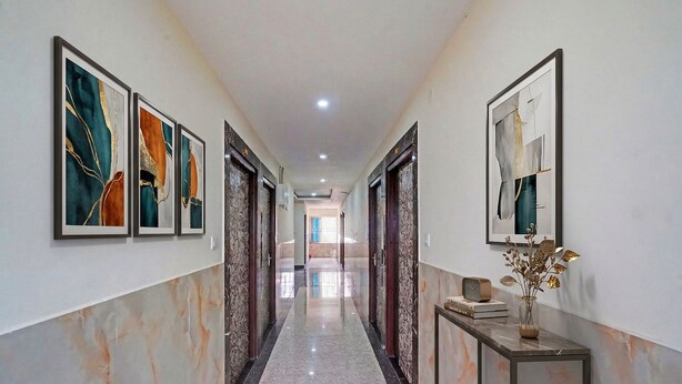 Um corredor com paredes de mármore, obras de arte emolduradas e um aparador com um vaso e livros.