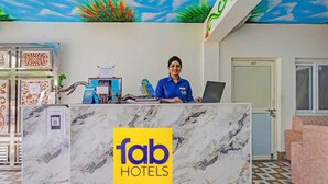 Bancada de recepção com o logotipo 'fab hotels', uma decoração de papagaio e um porta-etiquetas.