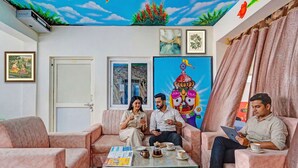 Quarto com sofá, mesa de centro com xícaras e um livro, porta e parede com um quadro.