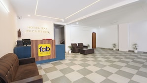 A hotel reception area with a checkered floor, a reception desk, a brown sofa, and two potted plants. - Fabhotel Sky Sector 76 (Gurugram)