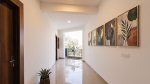 A hallway with a wooden door, a potted plant, and framed artwork on the wall. - Fabhotel Sky Sector 76 (Gurugram)