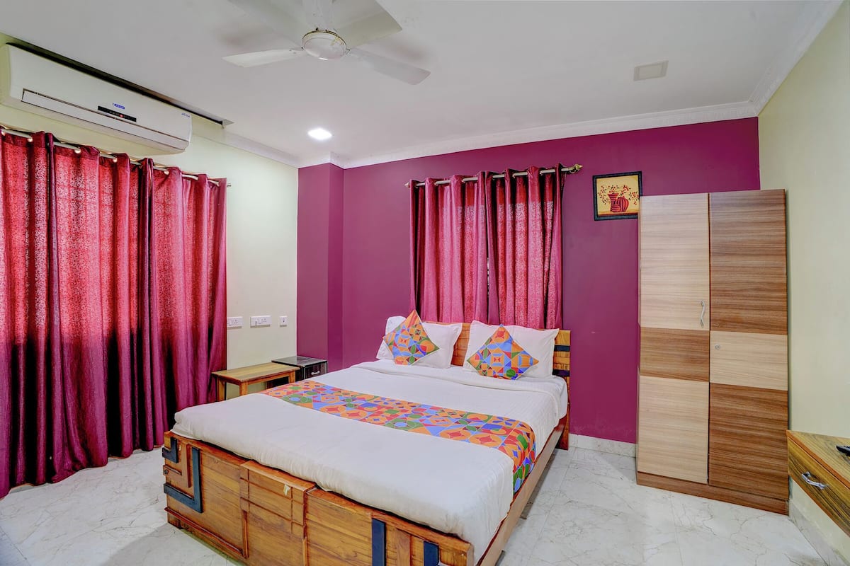 Une chambre à coucher comprenant un lit, des rideaux, un climatiseur, un ventilateur de plafond, une armoire et une petite table.
