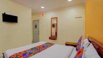 Habitación de hotel con una cama, un televisor montado en la pared, una puerta, un espejo y una mesita.
