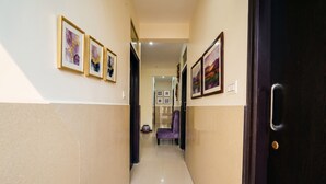 A hallway with framed artwork on the walls, a purple chair, and a dark wooden door. - Fabhotel Wagtail - Opp Wipro Corporate Office, Sarjapur (Bangalore)