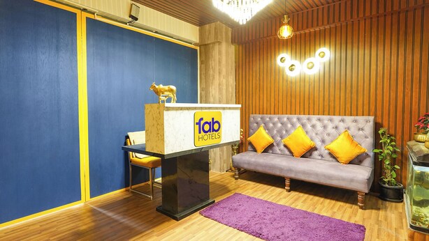 A reception desk with a sign, a sofa with yellow cushions, a chandelier, and a wooden wall. - Fabhotel Wagtail - Opp Wipro Corporate Office, Sarjapur (Bangalore)