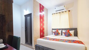 A hotel room with a bed, a desk, a chair, a wardrobe, and an air conditioning unit. - Fabhotel Wagtail - Opp Wipro Corporate Office, Sarjapur (Bangalore)