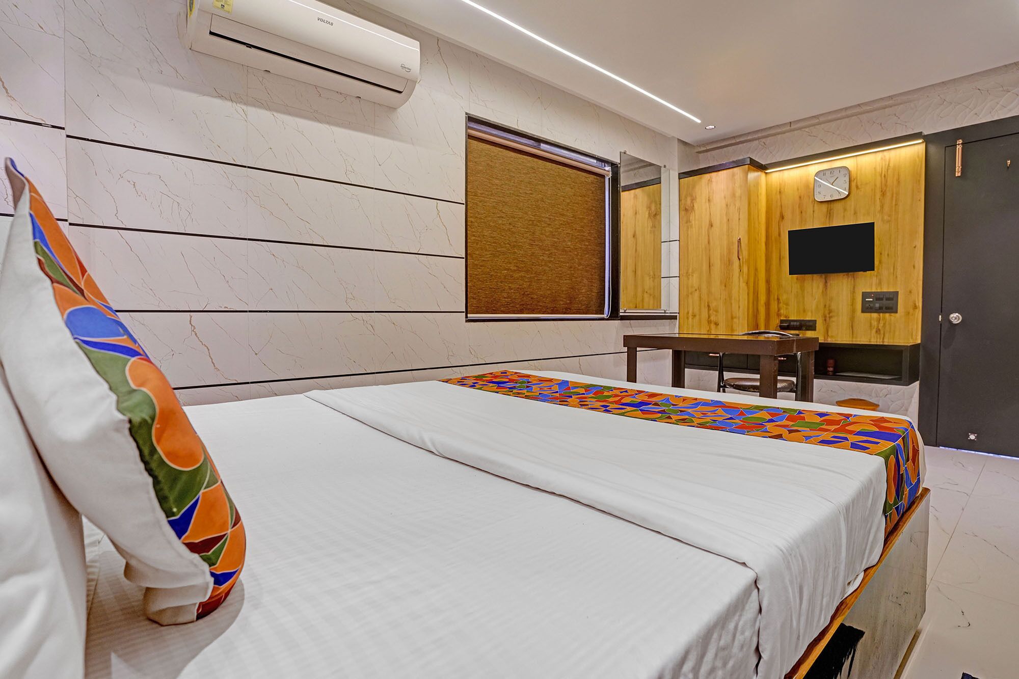 A hotel room with a bed, a desk, a chair, a television, and a wardrobe.