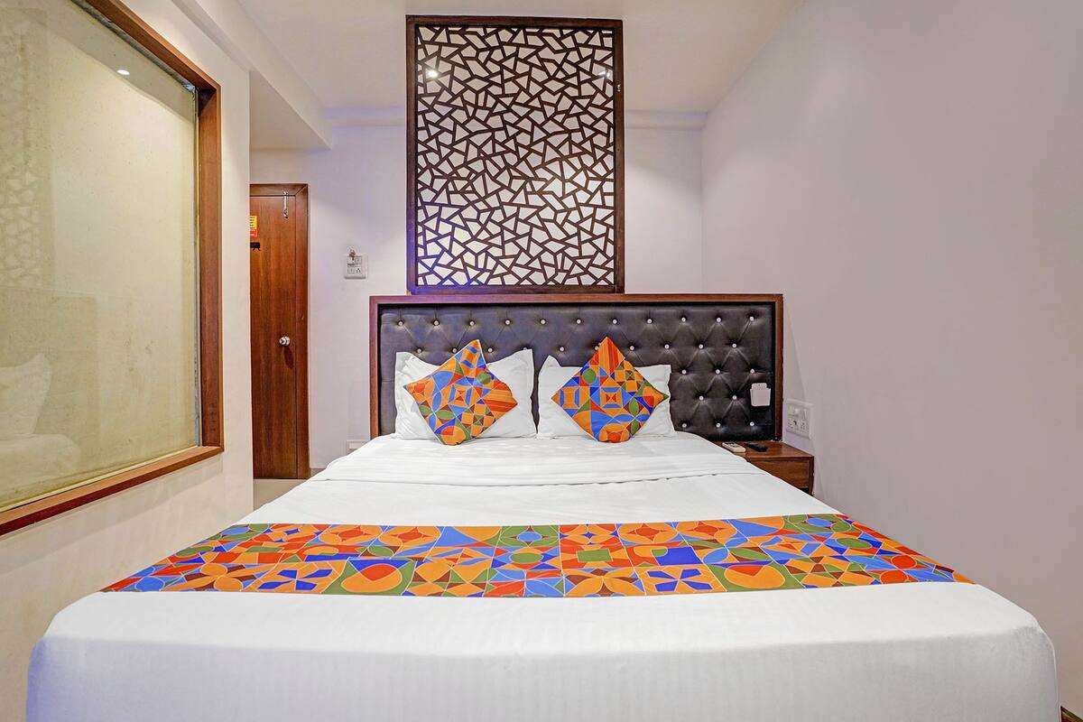 Ein Hotelzimmer mit einem Bett, einem verzierten Kopfteil, einer Bettdecke mit geometrischem Muster und einer Wandplatte.