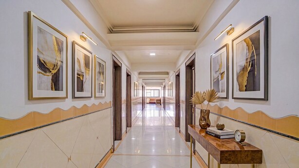 A hallway with framed artwork on the walls, a wooden console table with a clock and books, and a bench in the distance. - Fabhotel Dukes Plaza (Mumbai)