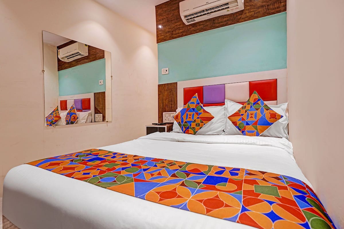 A hotel room with a bed, a mirror, and an air conditioning unit.
