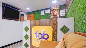 A reception area with a sign reading 'fab hotel,' a wooden reception desk, a green wall with artificial grass, and a television mounted on the wall. - Fabhotel Orange Residency (Mumbai)