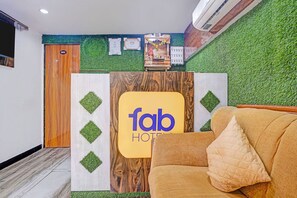 A reception desk with a wooden and white design, a 'fab' logo, and a green wall with grass-like texture. - Fabhotel Orange Residency (Mumbai)