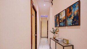 A hallway with a marble floor, a console table with a vase and books, and abstract paintings on the wall. - Fabhotel Orange Residency (Mumbai)