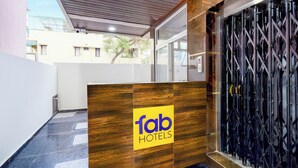 A reception desk with a 'fab hotels' logo, a glass door with a metal security gate, and a view of buildings in the background. - Fabhotel Golden City Inn (Hyderabad)